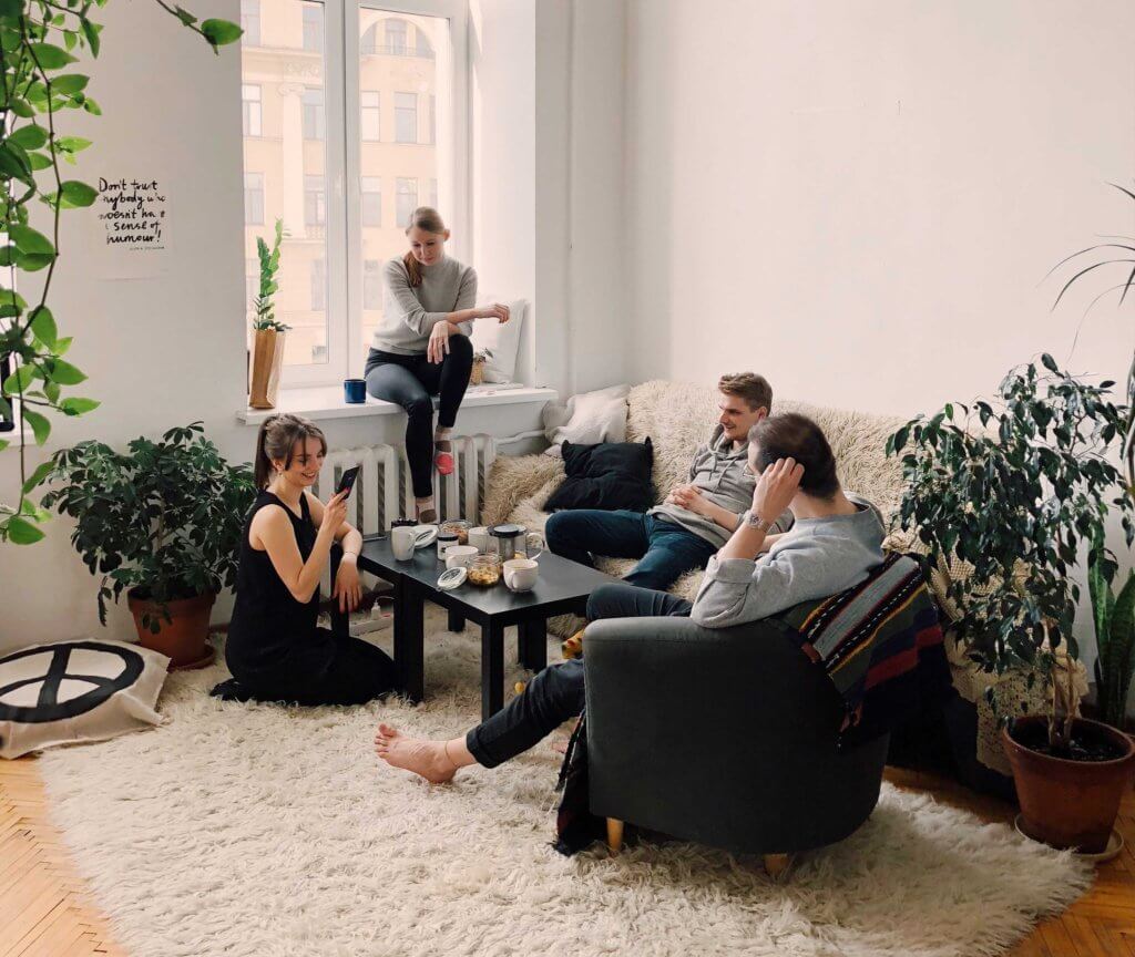 A group of people sat in a lounge on chairs and a sofa surrounding a coffee table with mugs on