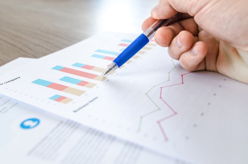 A piece of paper with a charts and graphs on and a hand holding a pen above it
