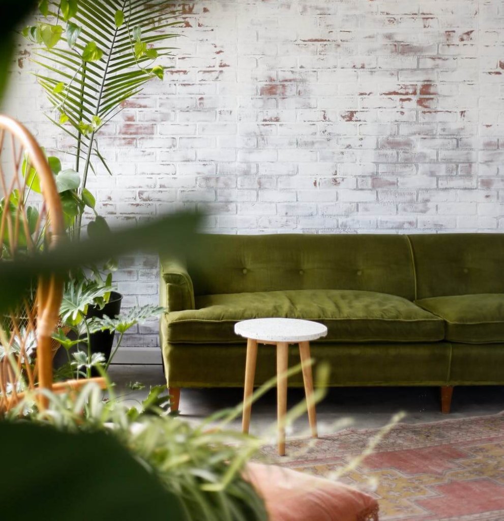 A green sofa and a stool by a window