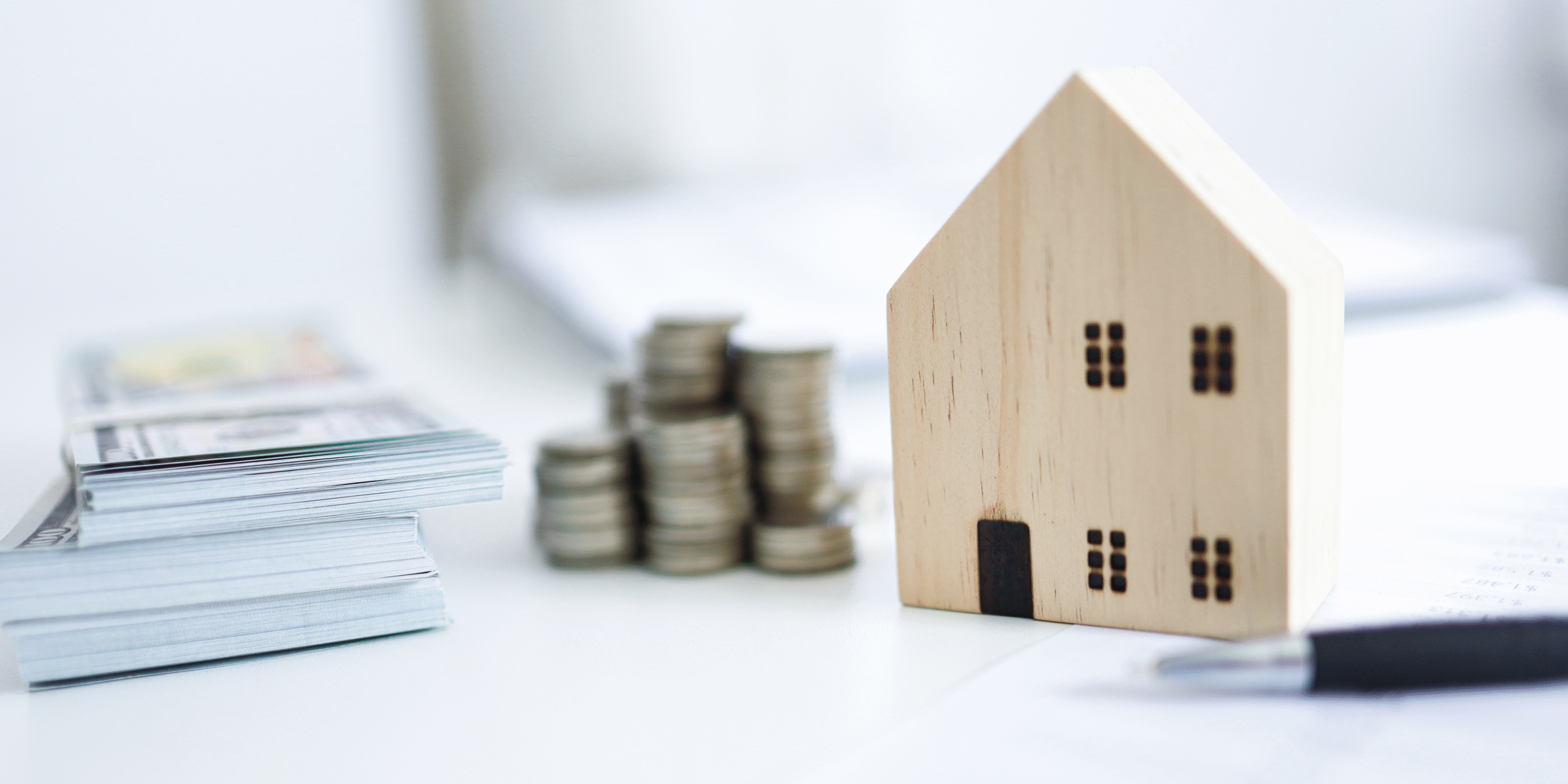 Close up of money, pen and toy wooden house on desk. 