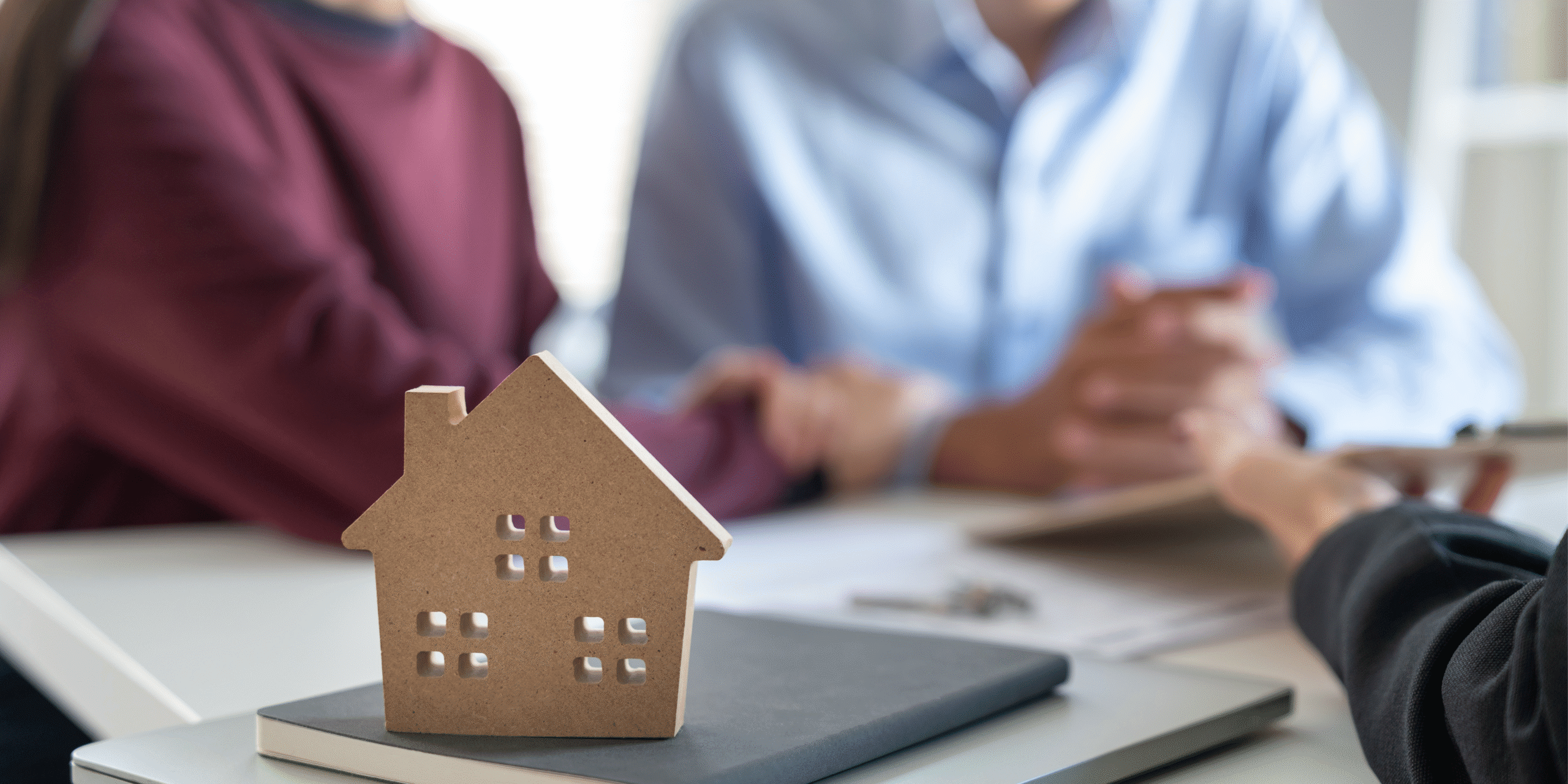 couple having meeting with estate agent. House figure that is sat on the desk is the main focus point.