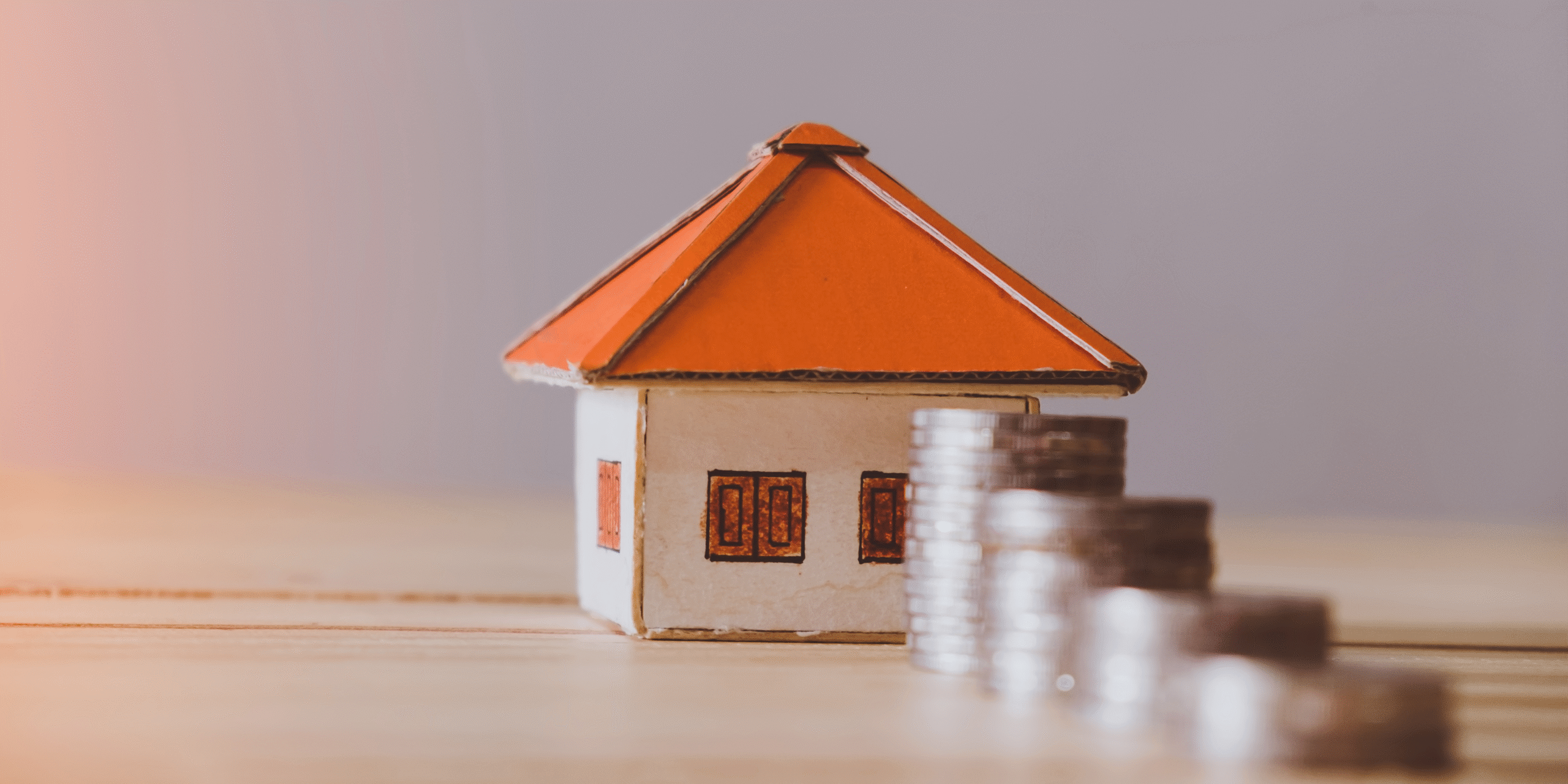 Model house on desk with coins stacked beside it. 