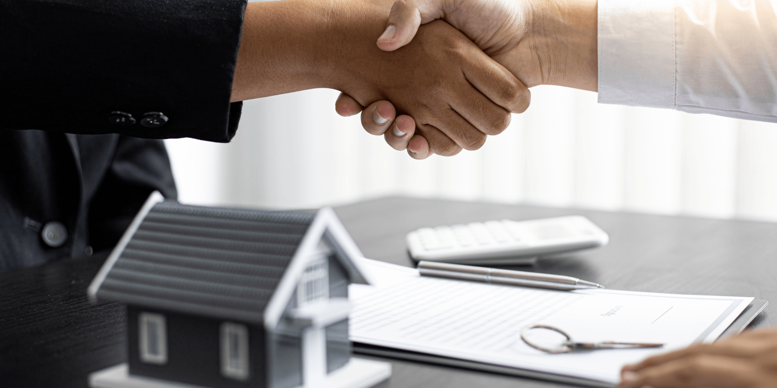 A handshake with a table of documents and a model house